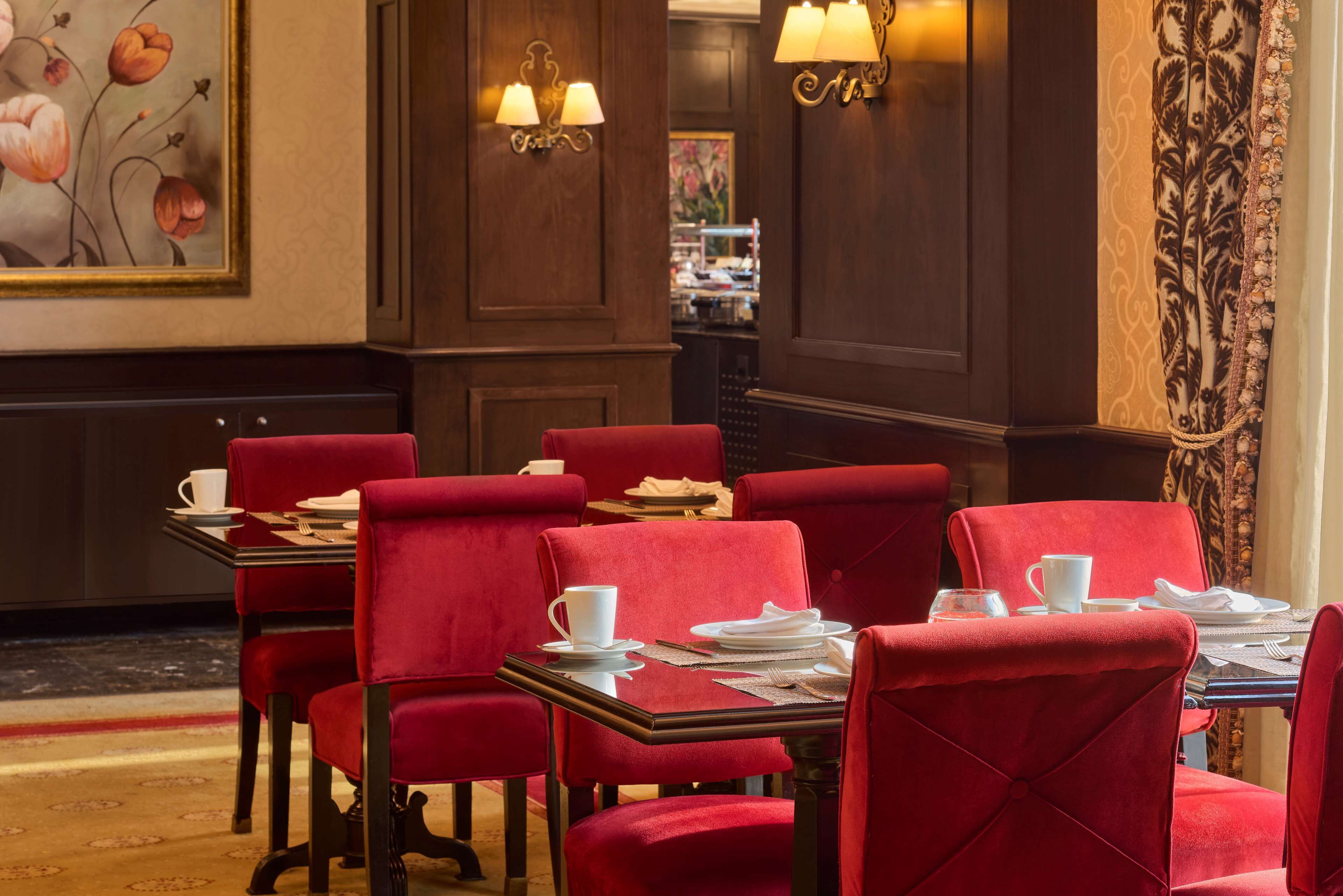 A dining area with red upholstered chairs, white table settings, and wall-mounted lamps.