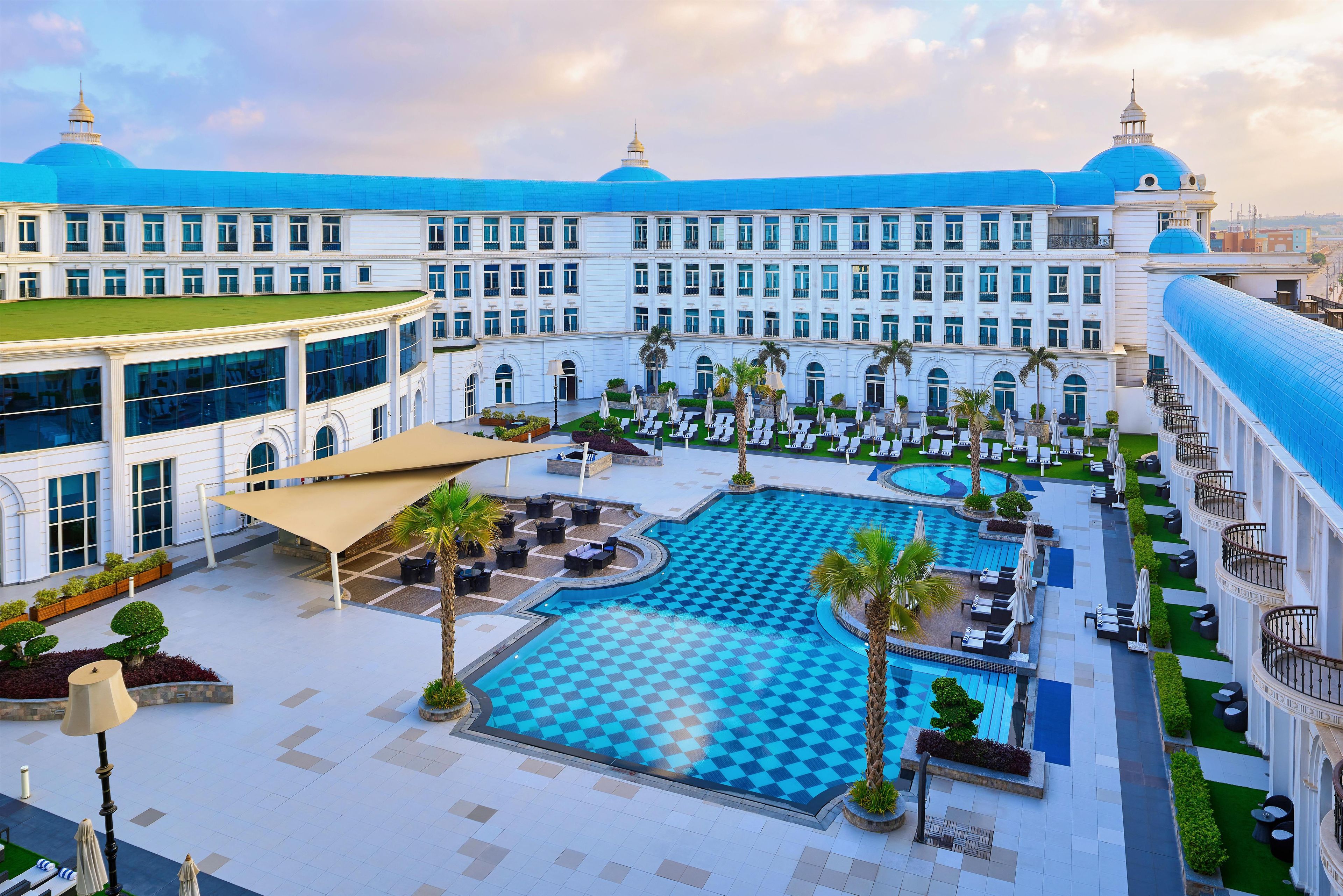 Un patio de hotel con una piscina amplia, zonas de descanso y un edificio imponente con cúpulas.