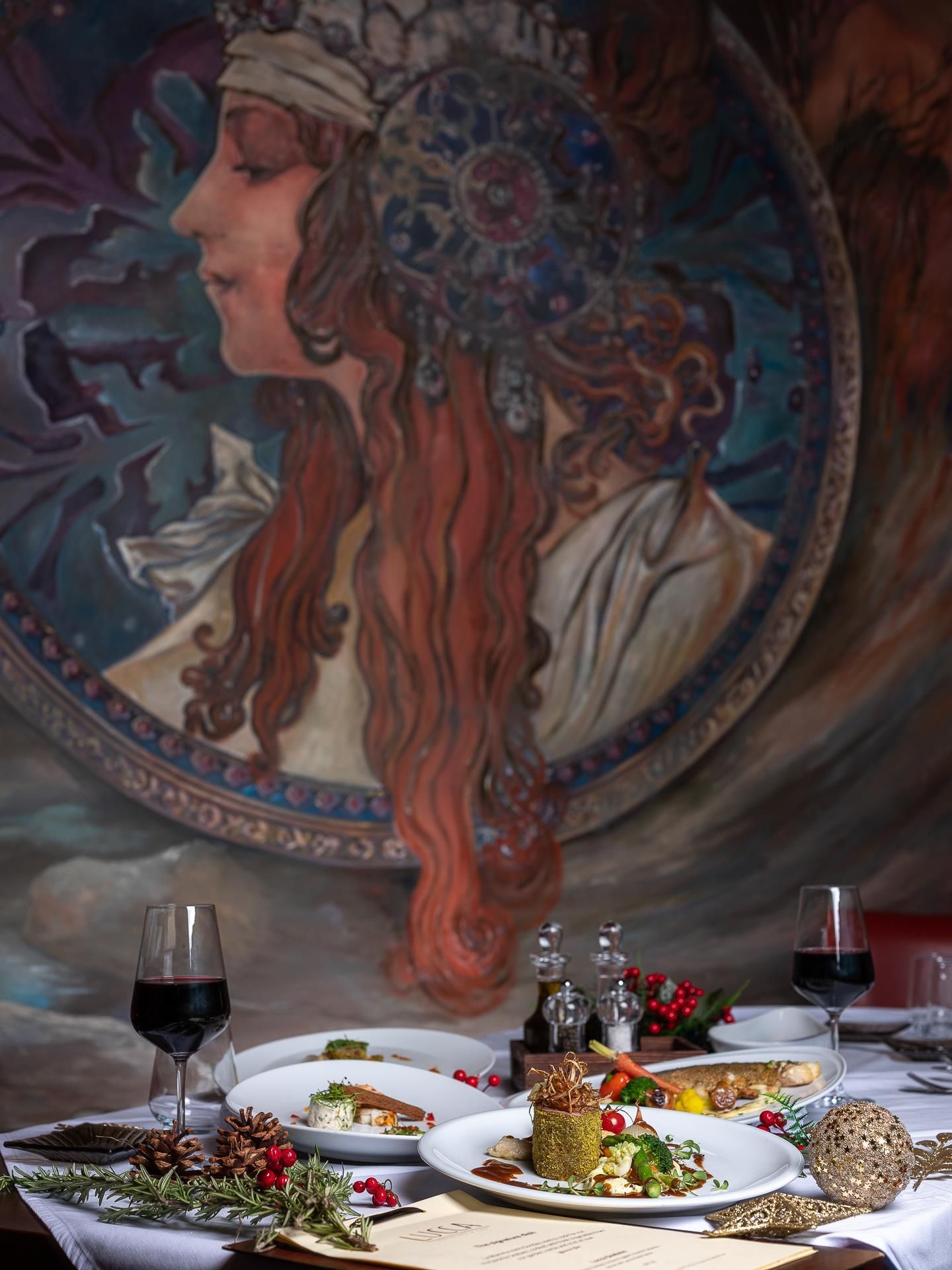 Une table à manger avec des assiettes remplies de nourriture, des verres de vin rouge et un menu.
