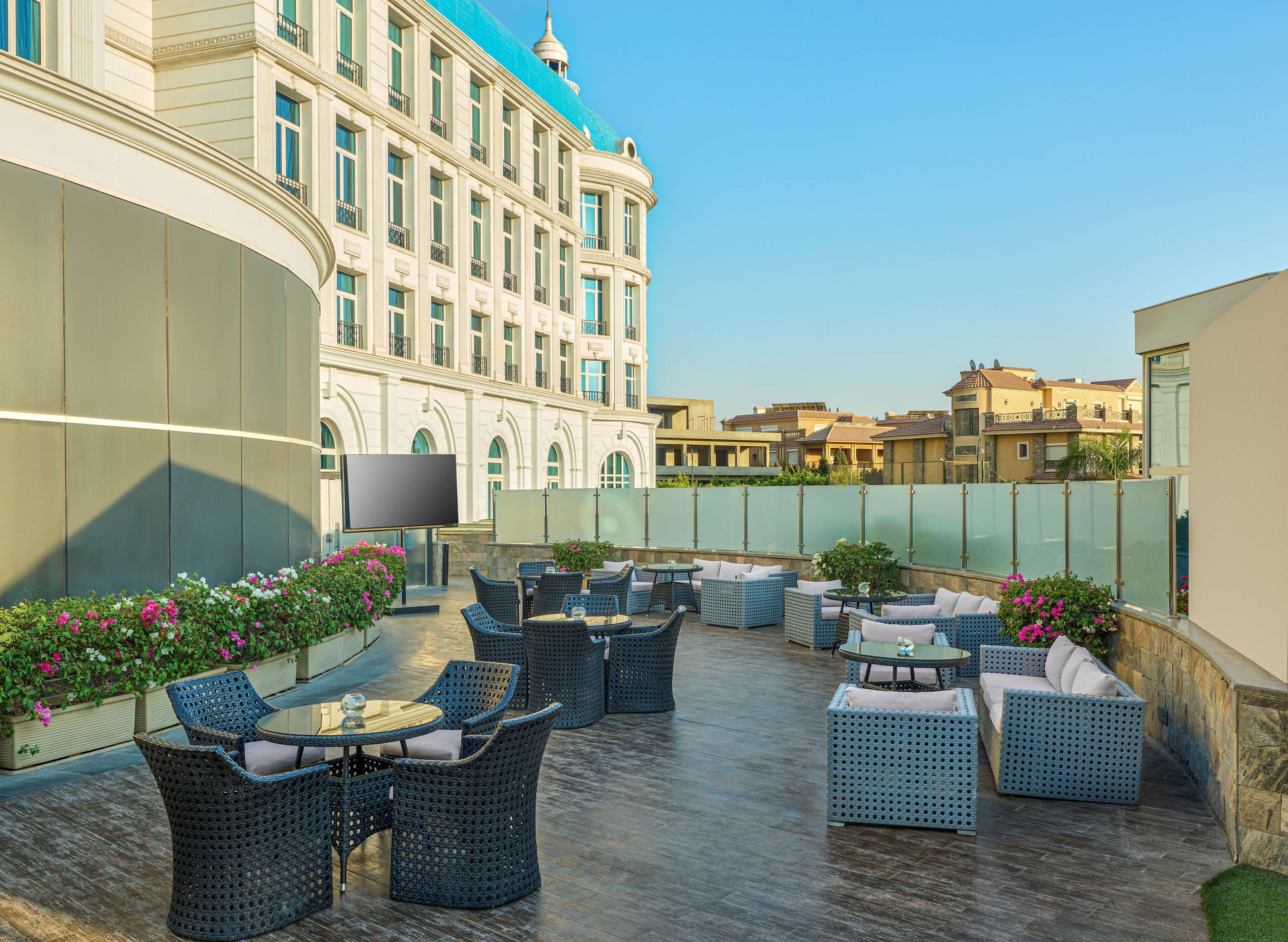 Une terrasse extérieure avec des meubles en osier et un grand bâtiment en arrière-plan.