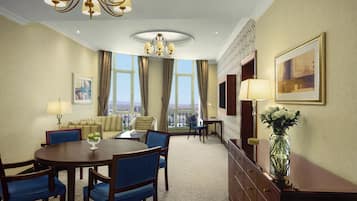 A hotel dining area with a round table, blue chairs, a chandelier, and a view through large windows.
