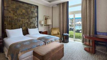 A hotel room with two beds, a sofa, a small table, a lamp, and a view of the pool and building.
