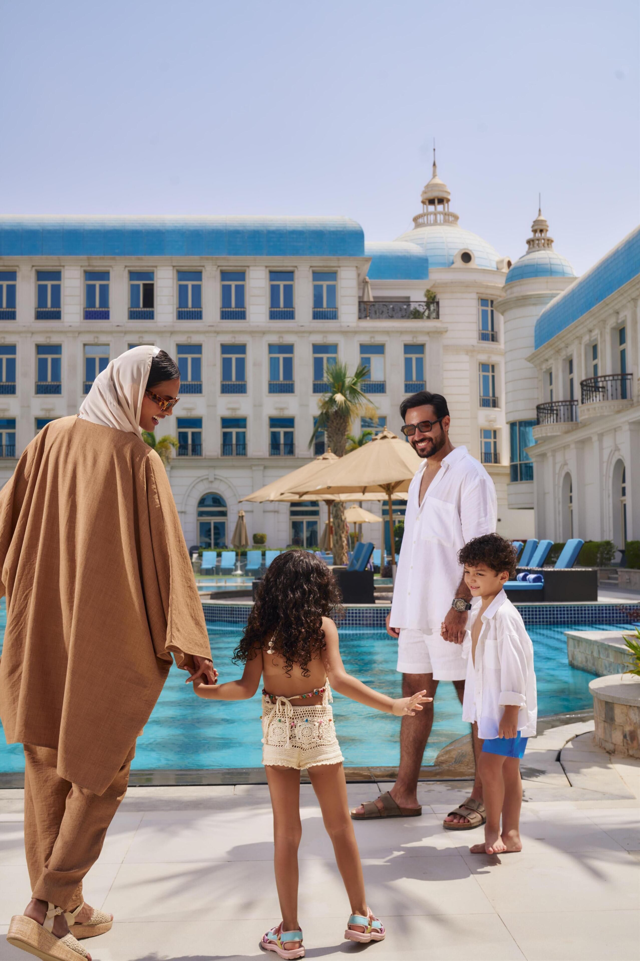 A family by a pool with a large building in the background.