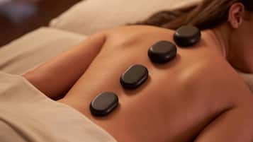 Une personne reçoit un soin du dos qui consiste à appliquer plusieurs pierres noires sur le dos.
