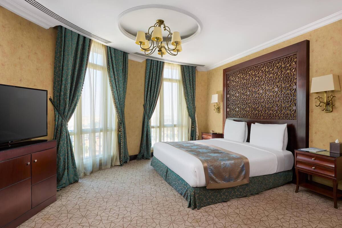 A hotel room with a large bed, a television on a cabinet, a chandelier, and a decorative wall panel.