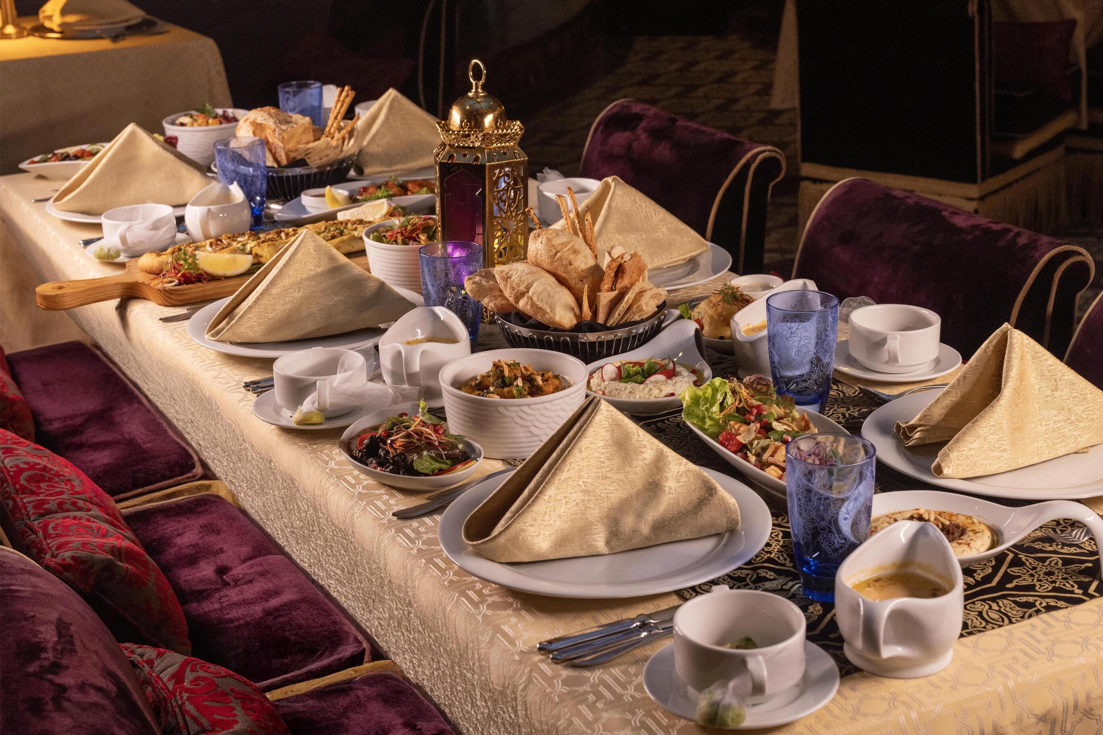 Une longue table à manger, dressée avec de nombreuses assiettes, des bols, des verres et des serviettes.