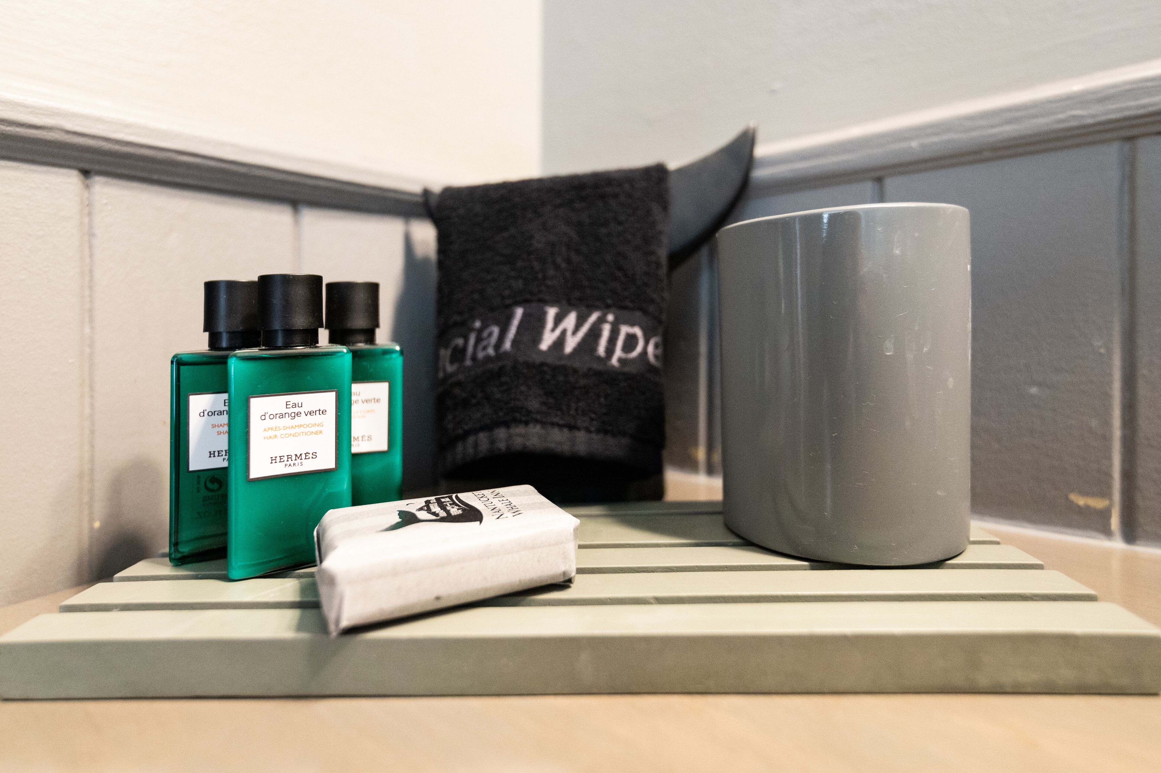 A bathroom shelf with a green bottle, a white bar of soap, and a gray mug.