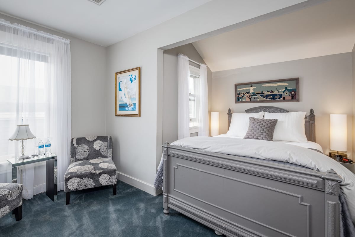 A hotel room with a bed, a chair, a desk, and a window with curtains.