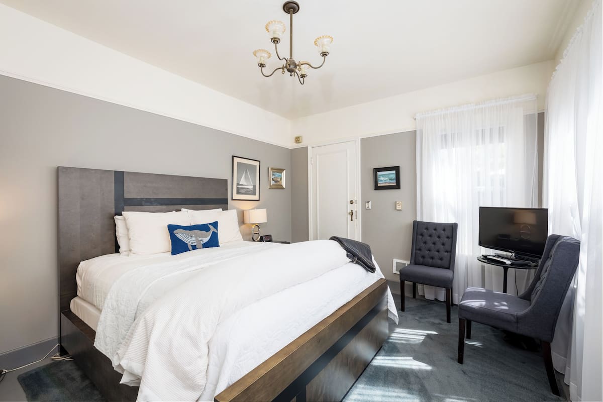 A hotel room with a large bed, a television, a chair, and a desk.
