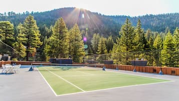 An outdoor tennis court with a net, surrounded by trees and a mountain in the background.