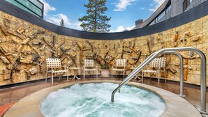 Ein Whirlpool vor einer Wand aus Stein, umgeben von Stühlen und einem kleinen Tisch.
