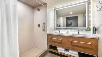 A modern bathroom with a walk-in shower, two sinks, a large mirror, and a towel rack.