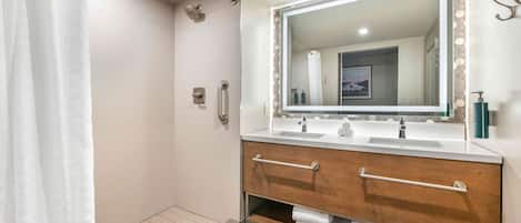 A modern bathroom with a walk-in shower, two sinks, a large mirror, and a towel rack.