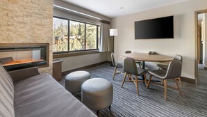 Ein Hotelzimmer mit Steinwand, Kamin, großem Fenster, Flachbildfernseher, rundem Tisch mit Stühlen und einer Couch.