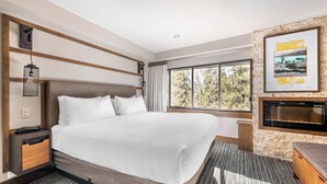 Ein modernes Hotelzimmer mit einem großen Bett, einem Kamin, einem Schreibtisch und einem Fenster mit Blick auf Bäume.