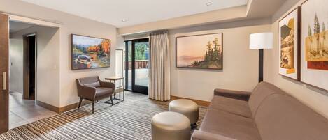 A modern hotel room with a large window, a sofa, a chair, a small table, and two ottomans.