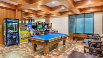 A room with a pool table, arcade games, and wooden paneling.