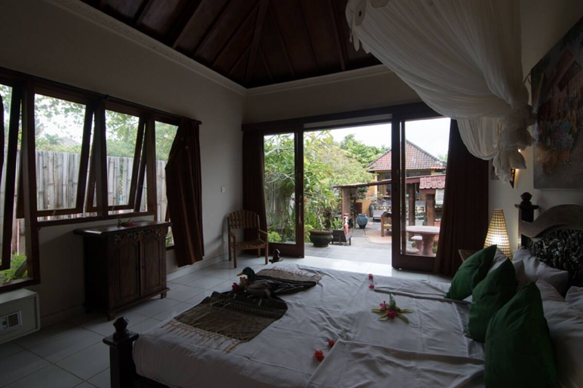 A bedroom with a bed, a chair, a desk, and a view of the outside.