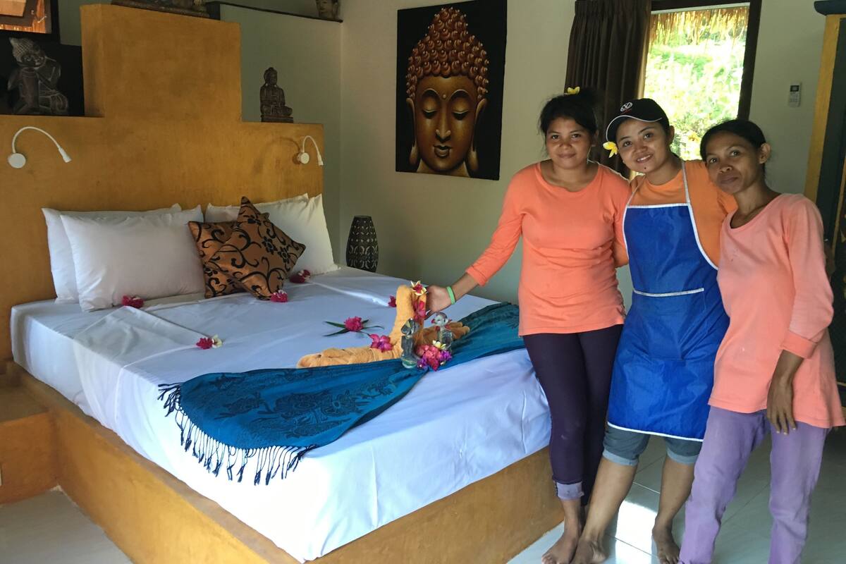 A bedroom with a bed, pillows, a Buddha statue, and a Buddha painting on the wall.