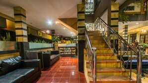 Un vestíbulo con piso de baldosas rojas, asientos de cuero negro, una escalera con barandillas metálicas y una estantería.
