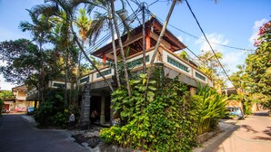 Un edificio tradicional con estructura de madera, rodeado de exuberante vegetación y una calle pavimentada.