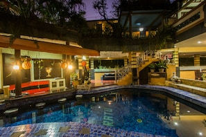 A swimming pool with a tiled floor, a bar area with stools, and a staircase leading to an upper level. - Sri Ratu Hotel (Legian)