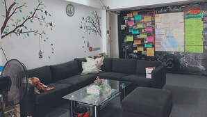 A room with a black sofa, a glass coffee table, and a wall decorated with a tree mural and a map of Thailand. - 1Sabai Hostel (Bangkok)