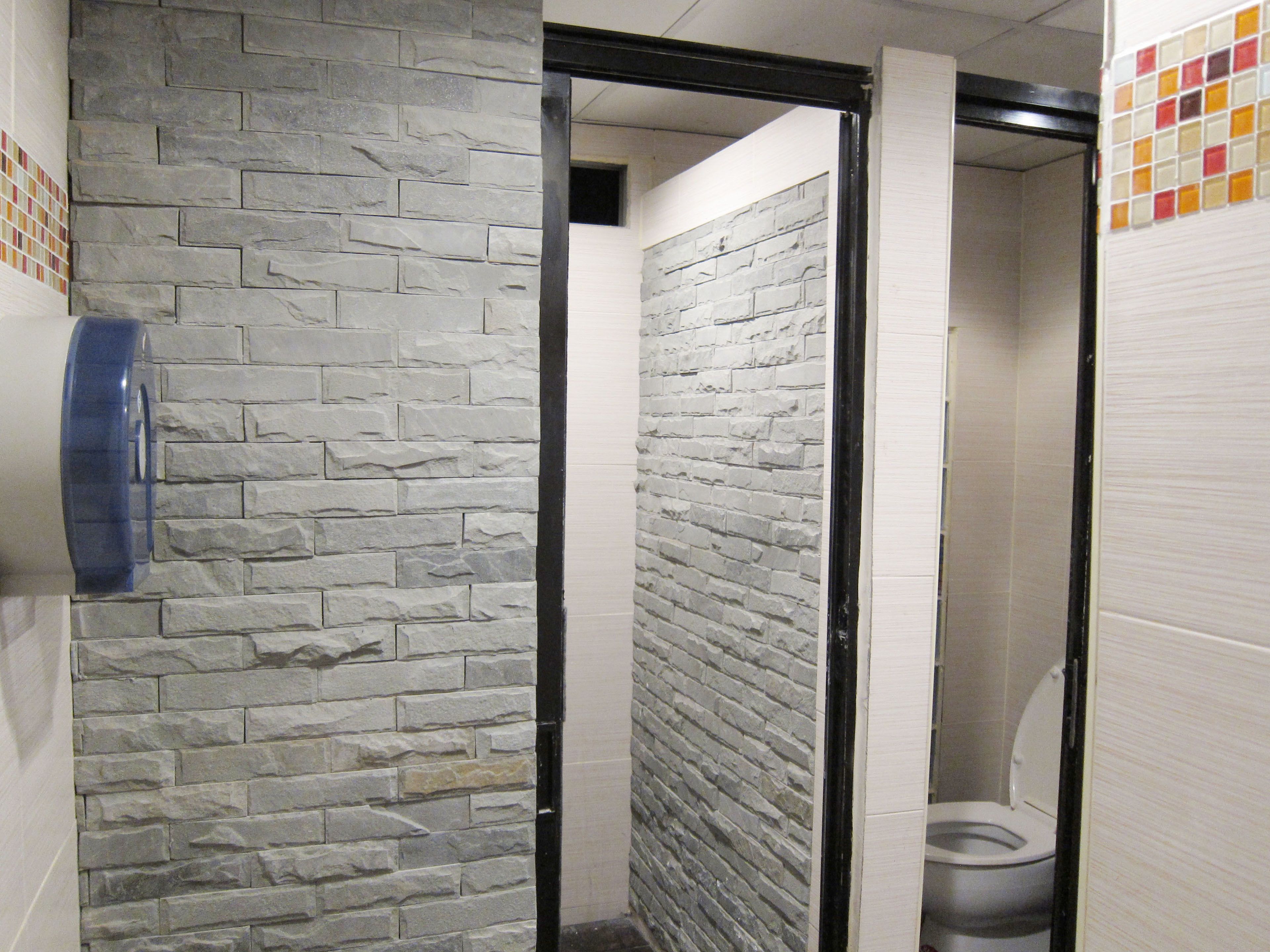 A bathroom with stone walls, a toilet, and a blue hand dryer.