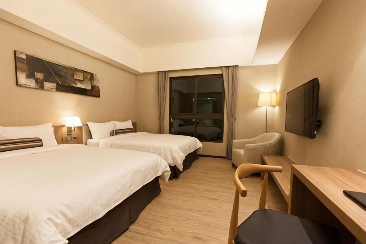 Une chambre d’hôtel avec deux lits, un bureau, une chaise, une télévision et une fenêtre avec des rideaux.