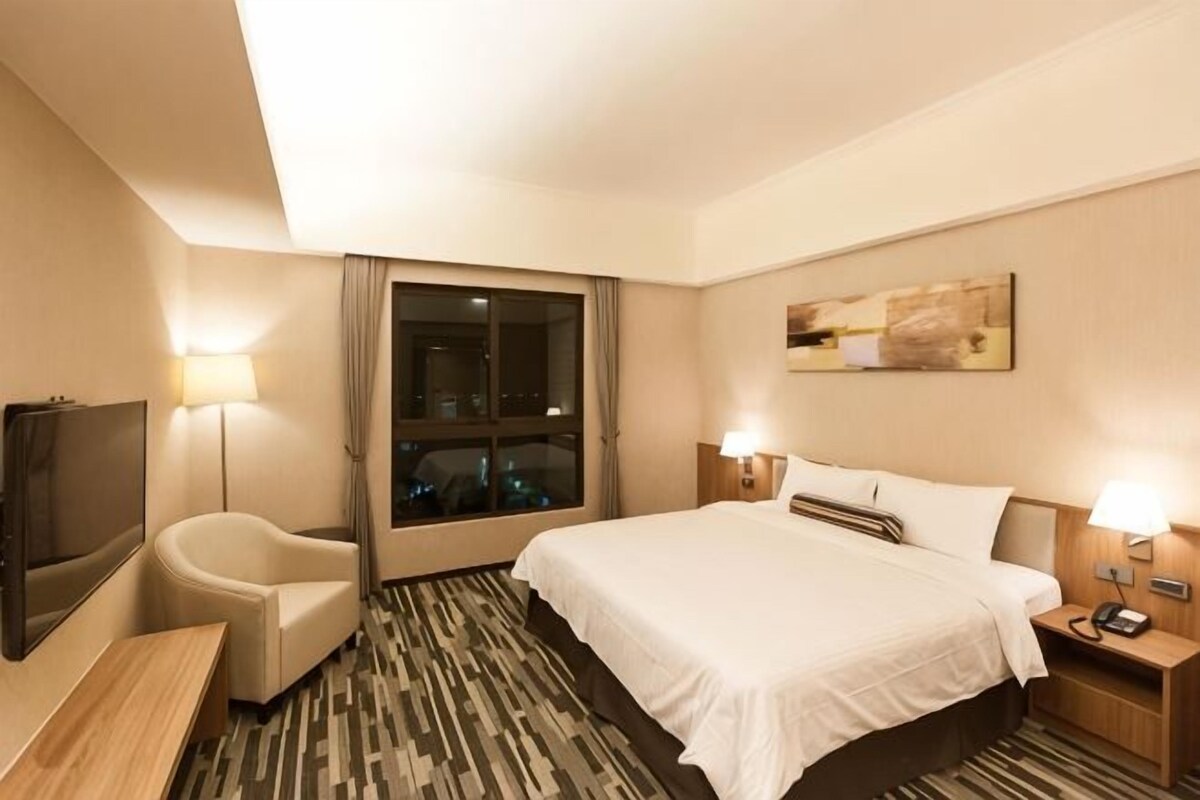 Une chambre d’hôtel équipée d’un lit, d’un bureau, d’une chaise, d’une télévision et d’une table de chevet avec une lampe.