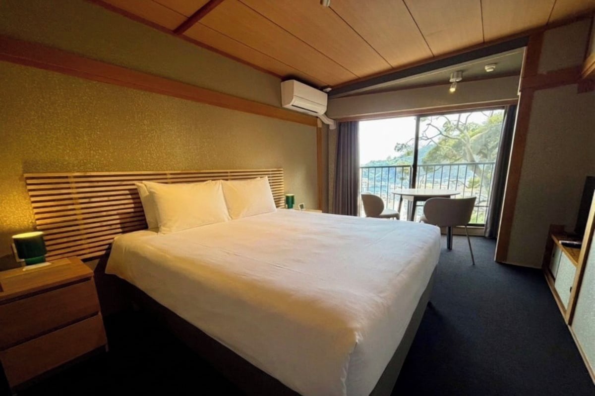 Une chambre d’hôtel avec un grand lit, une table de chevet, une chaise et une vue sur l’extérieur.