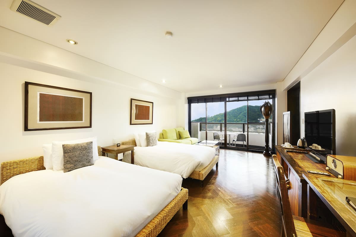 A hotel room with two beds, a sofa, a dining table, and a TV.