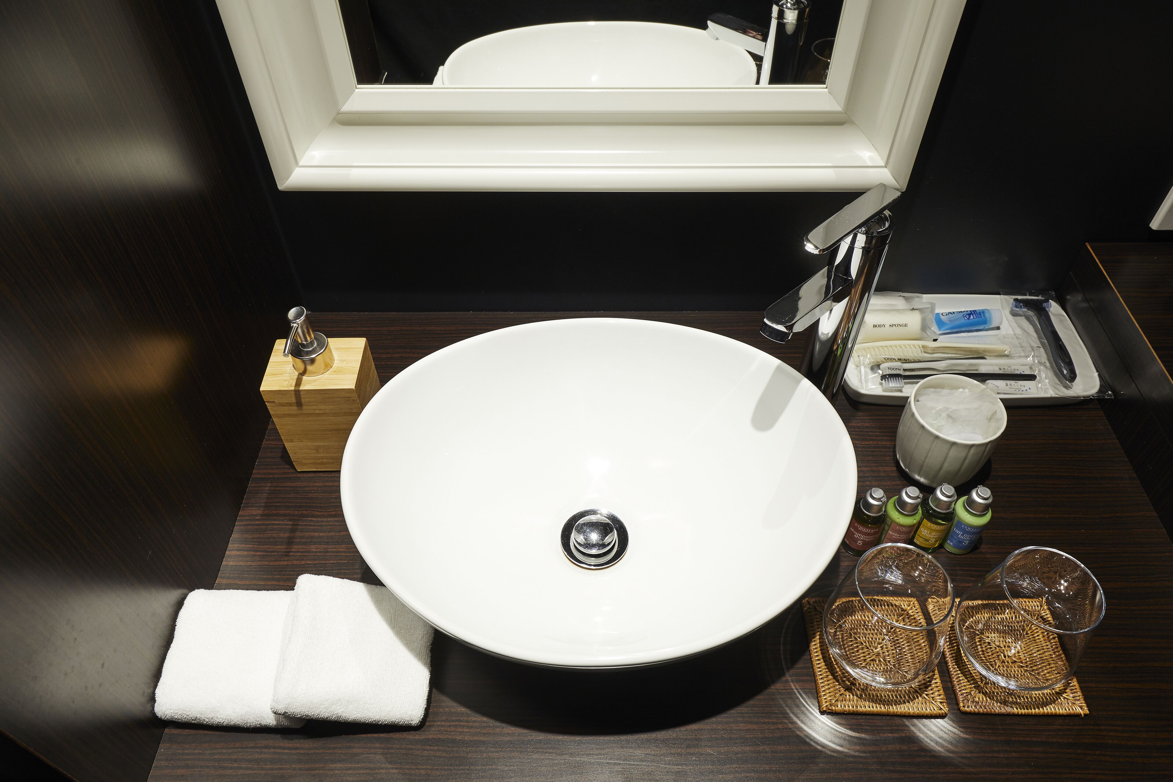A bathroom sink with a white basin, a towel, a toothbrush holder, a soap dispenser, and a tray with a toothbrush, toothpaste, and a cup.