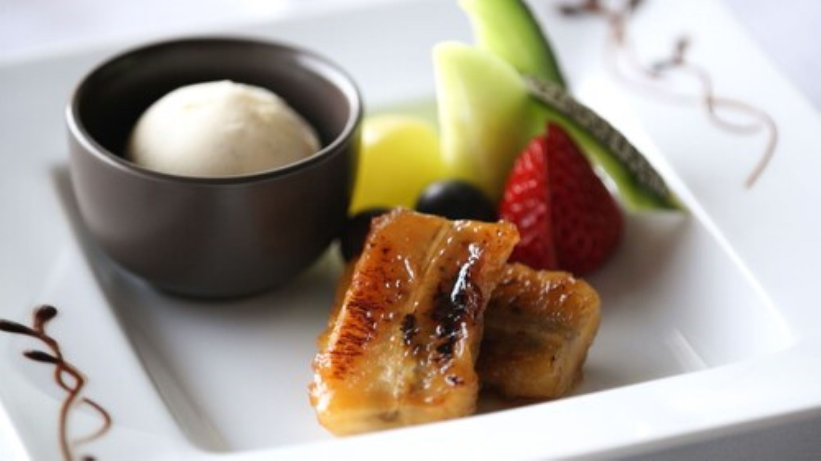 A plate with a piece of glazed meat, a bowl of ice cream, and assorted fruits.