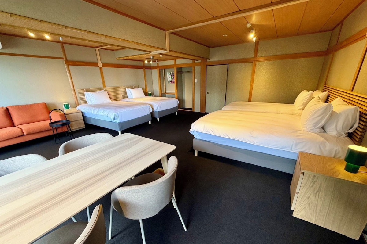 Une chambre d’hôtel avec un grand lit, deux petits lits, un canapé, une table à manger et des chaises.