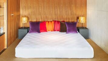 A large bed with a white mattress, surrounded by purple and red pillows, and two nightstands with lamps.