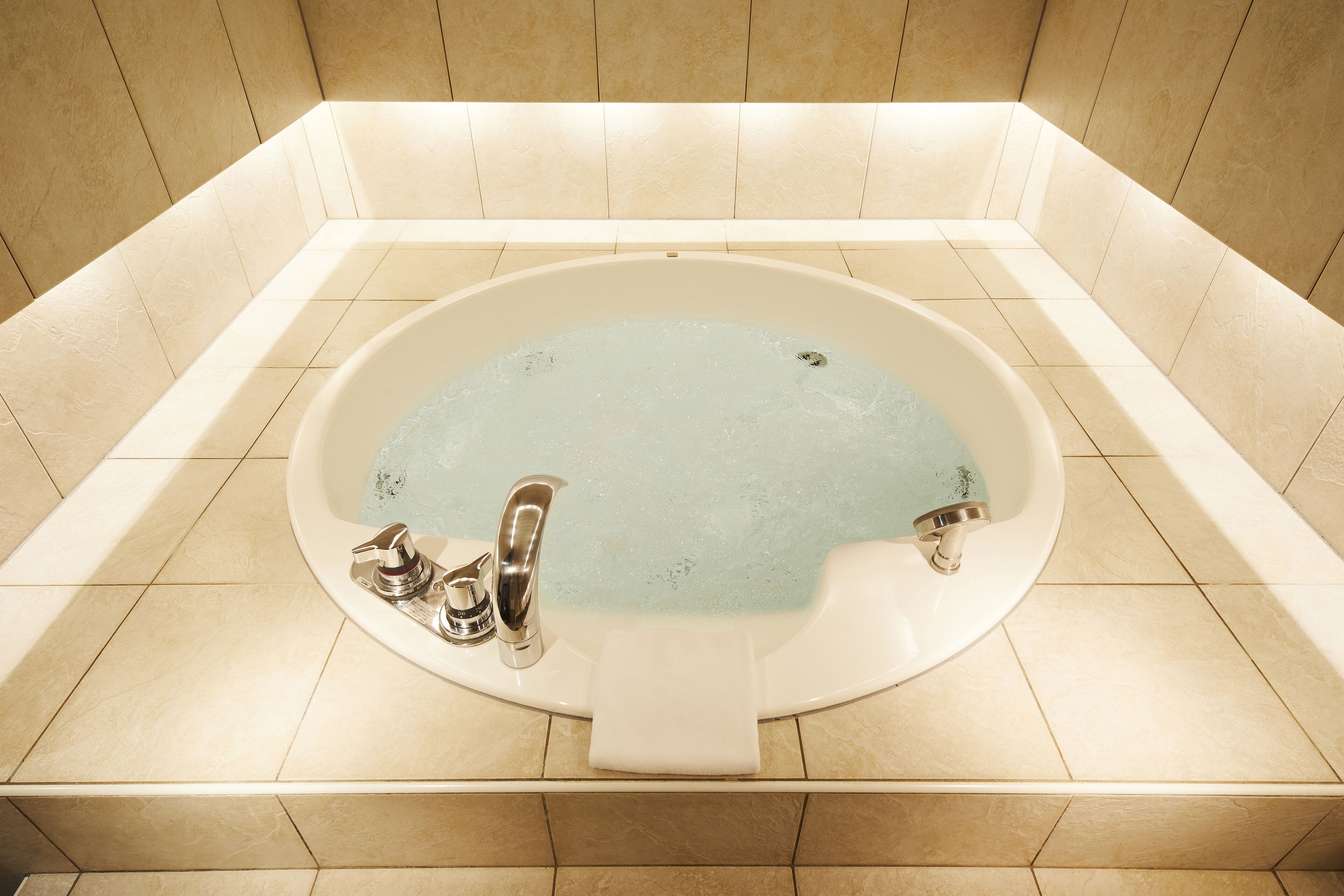 A large, oval-shaped bathtub with a single faucet and a built-in seat, surrounded by beige tiles.