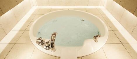 A large, oval-shaped bathtub with a single faucet and a built-in seat, surrounded by beige tiles.
