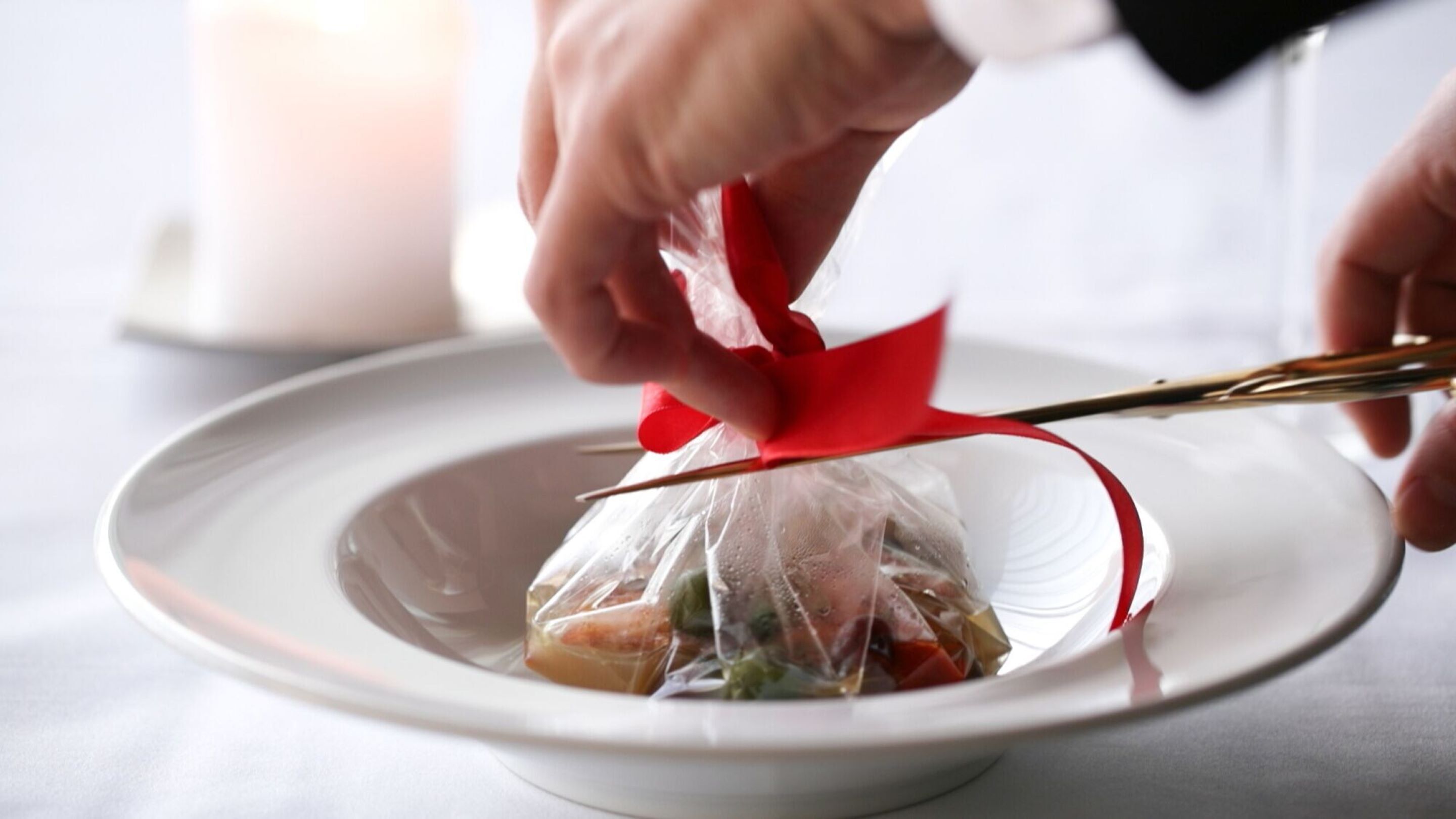 Une personne utilise des ciseaux pour couper un ruban rouge sur une assiette blanche contenant de la nourriture.