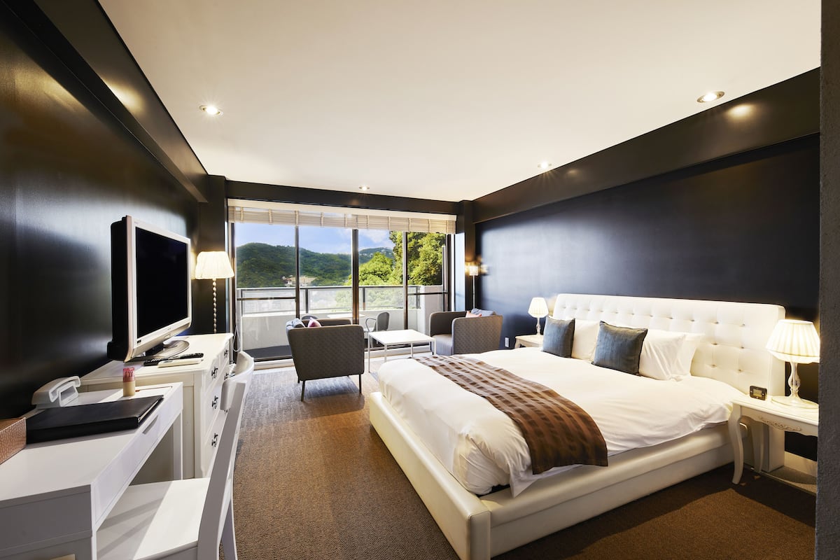 A modern hotel room with a large bed, a desk with a computer, a chair, and a TV.