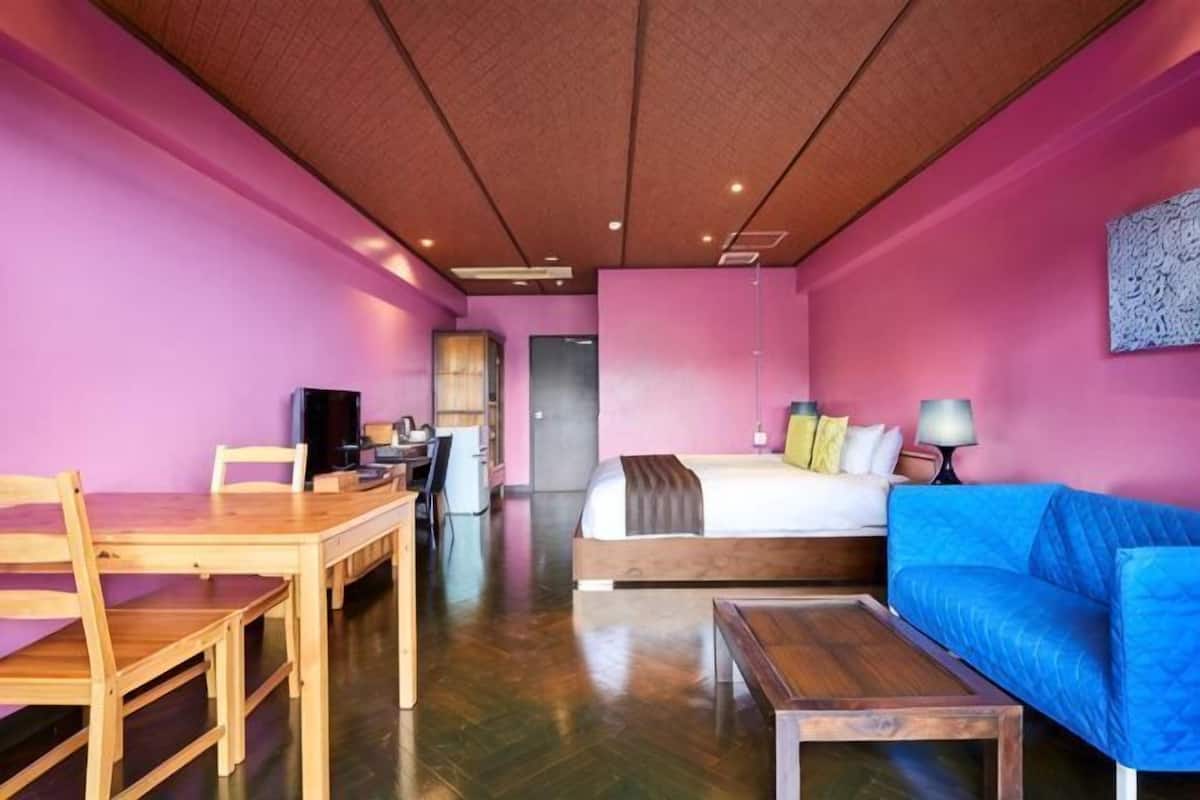 A room with a bed, a blue sofa, a wooden table, and a desk with a chair.