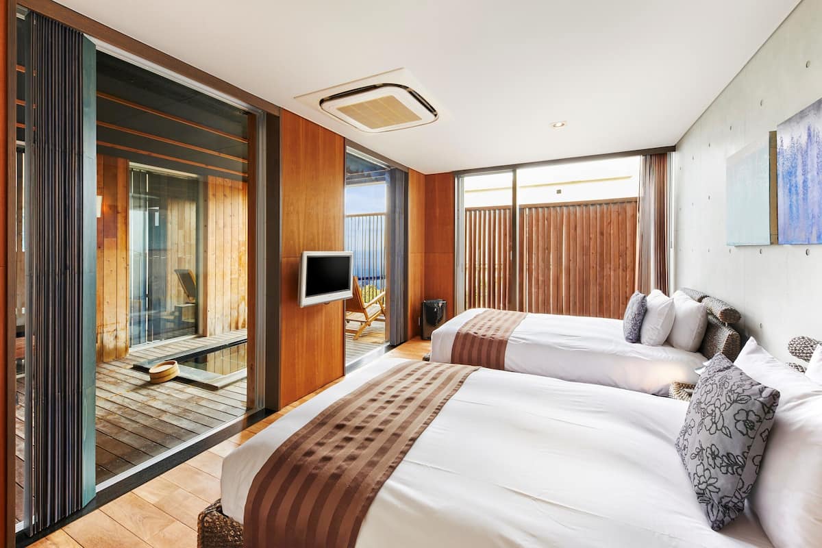A modern hotel room with two beds, a TV, and a balcony with a view.