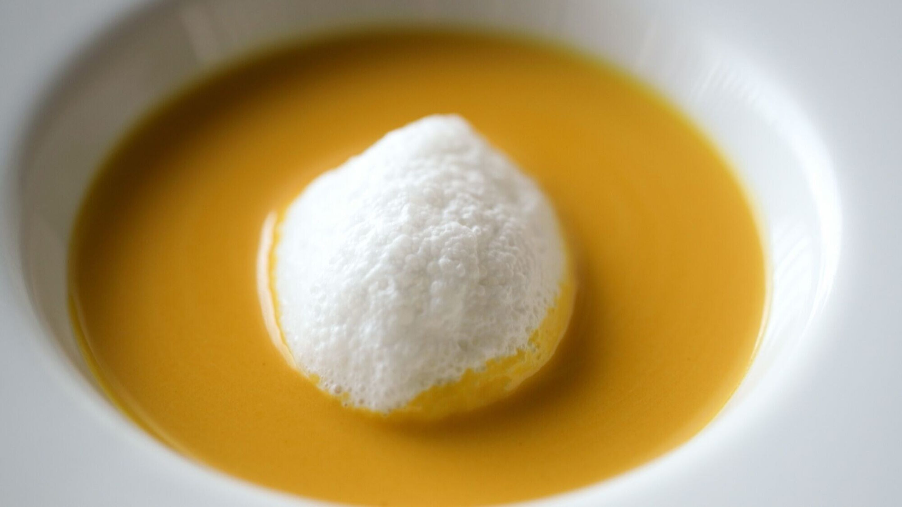 A dessert with a white topping in a yellow liquid.