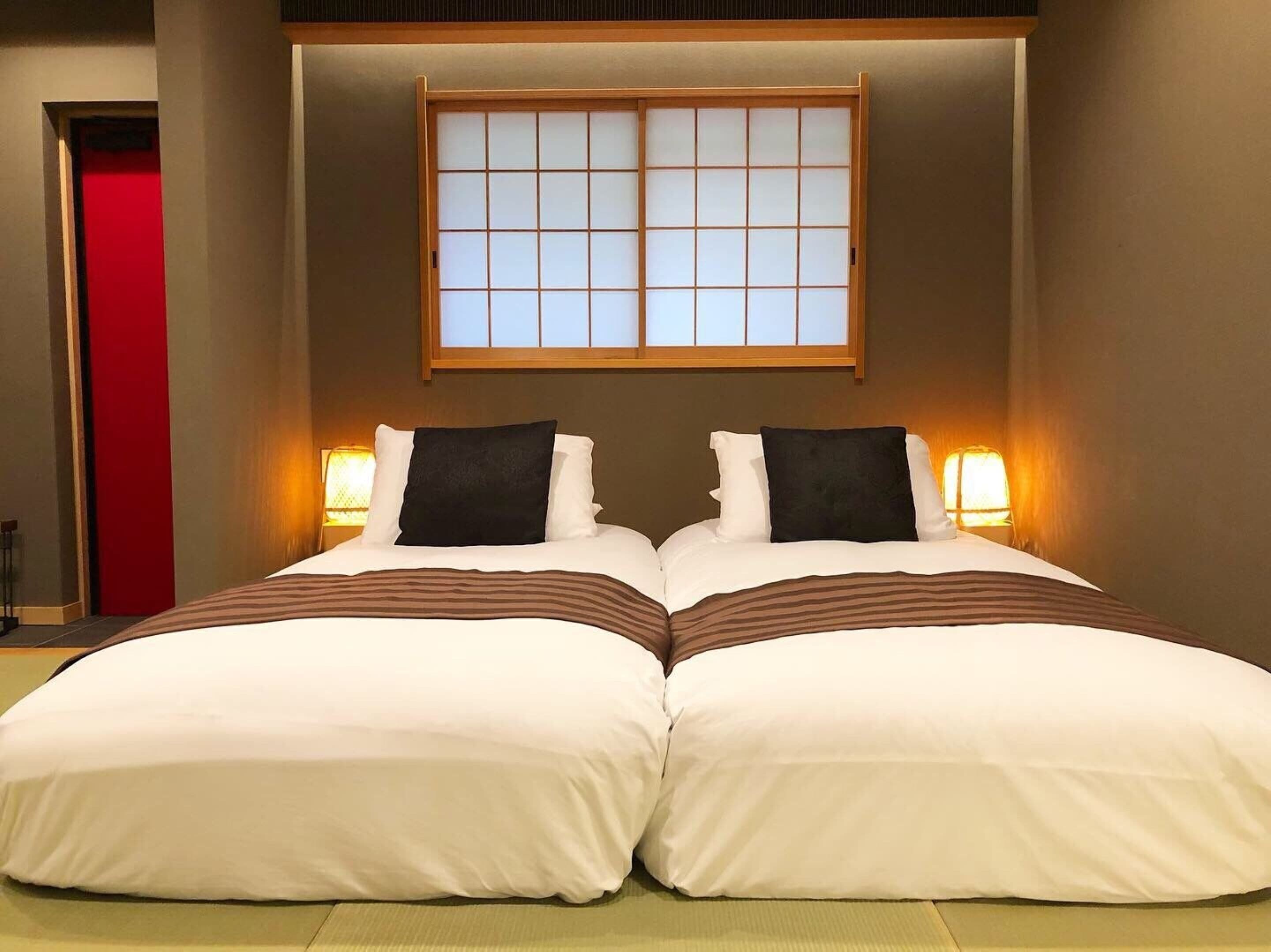 Een hotelkamer met twee bedden, een schuifdeur van shoji-scherm en bedlampjes.