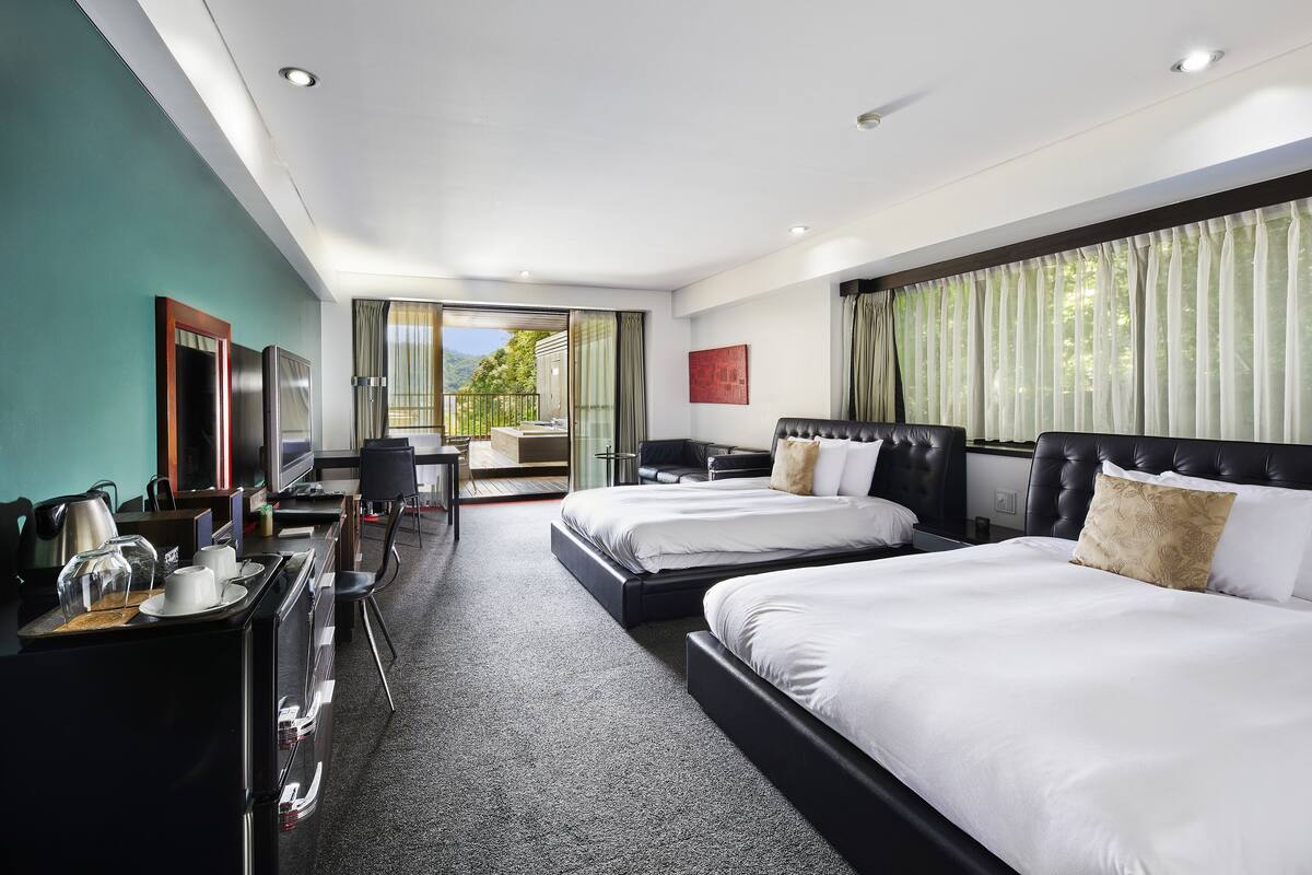 A hotel room with two beds, a desk, a chair, and a view of the outdoors.