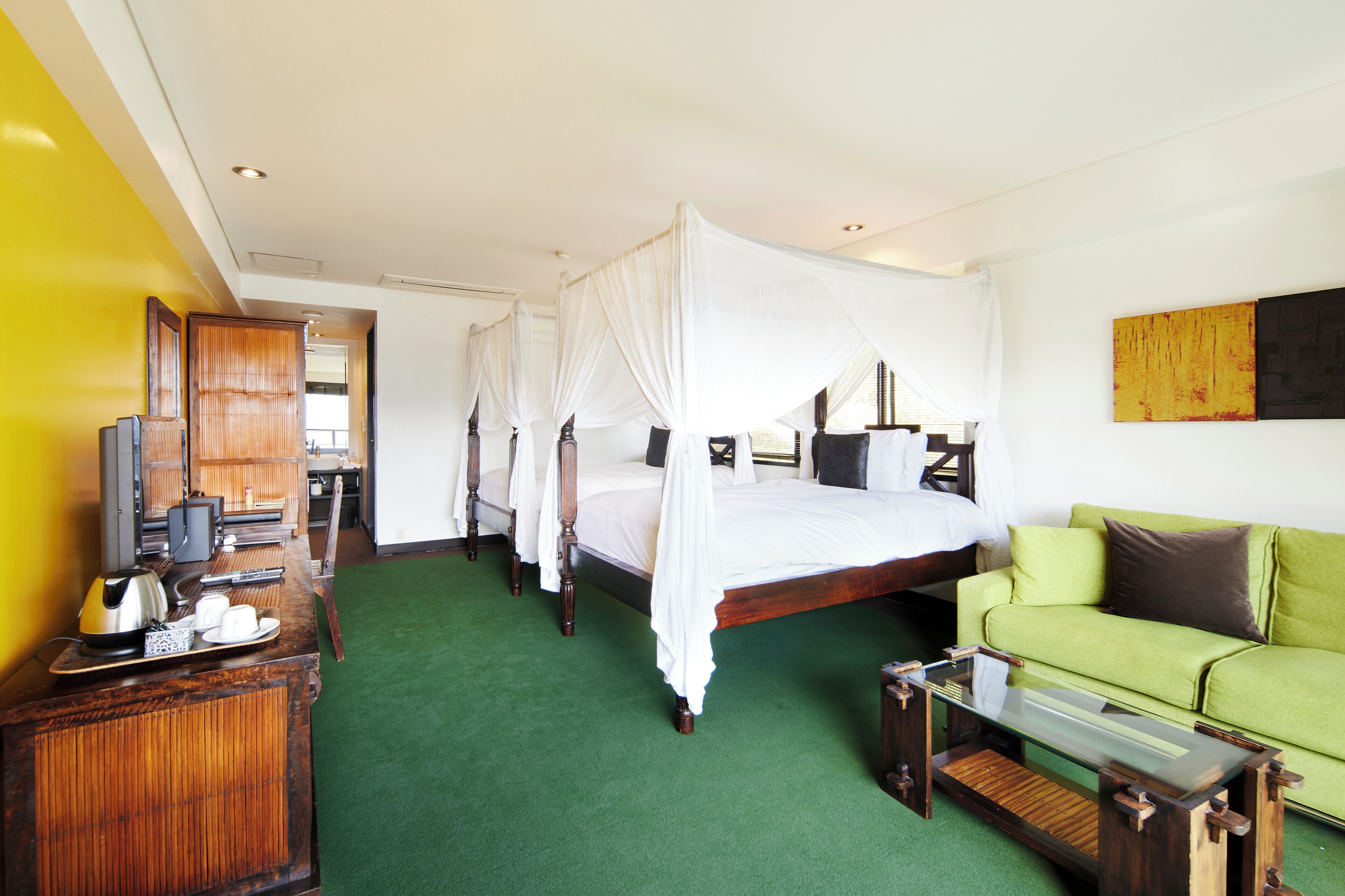 Een hotelkamer met een hemelbed, een groene bank, een houten bureau en een televisie.