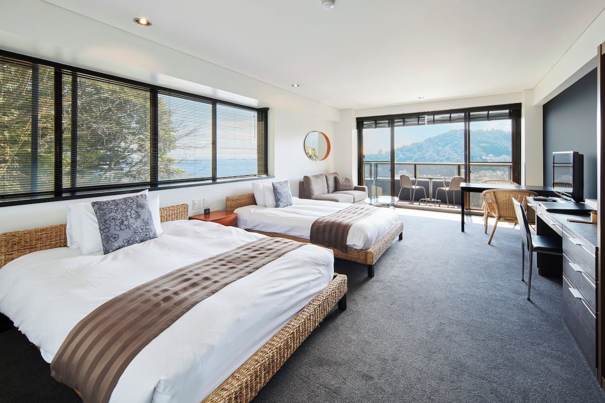 A modern hotel room with two large beds, a dining area, and a view of the mountains.