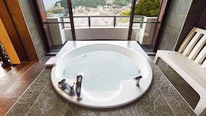 Une salle de bain dotée d’une grande baignoire, d’un banc et offrant une vue sur la ville et les montagnes grâce à de grandes fenêtres.
