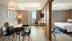 A hotel room with a bed, a desk, a sofa, and a dining area.