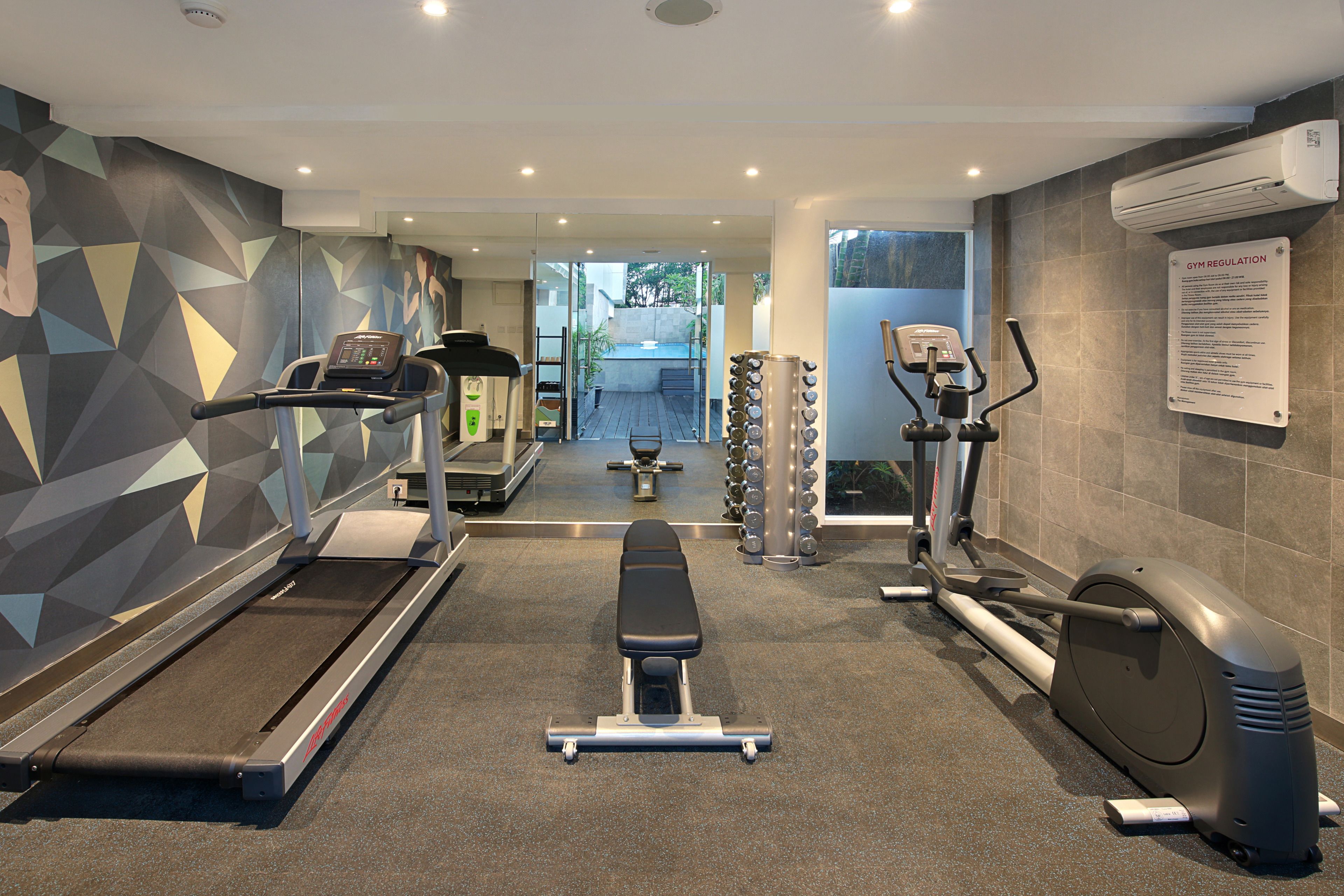 Une salle de sport équipée de tapis de course, d’un appareil elliptique, d’un banc de musculation et d’un climatiseur fixé au mur.